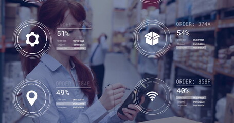Holding tablet with stylus, female worker scanning inventory in warehouse aisle, with digital icons