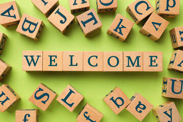 Word Welcome made of wooden cubes on light green background, flat lay