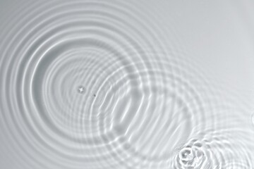 Water drops fall on calm clear transparent water surface creating sparkling texture water waves, circle rings, ripples, splashes and bubbles. For Summer Banner, product advertising, cosmetic, skincare
