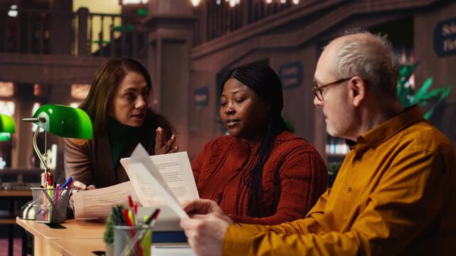 Mature team of performers rehearsing script dialogue together in a library, making drama play role preparations for character development. commitment to acting and dramaturgy. Camera B.