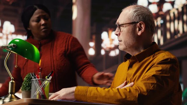 Senior adult in hyperventilation crisis feeling unwell in the campus library, having difficulty breathing and showing vulnerability. Old student having a panic attack emergency. Camera B.