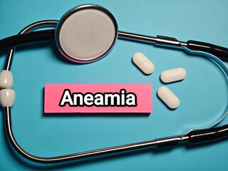stethoscope on a blue background with pills and word " Aneamia" 