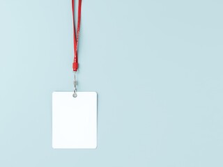 A blank white identification card hanging from a red lanyard against a light blue colored background
