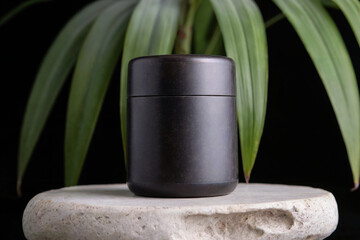 Naklejka premium A product photography shot of a matte black ceramic container on a light beige stone pedestal against a black background. 
