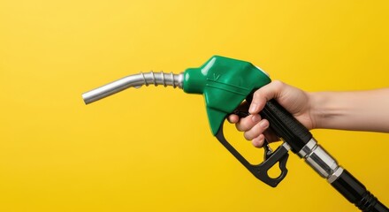 Photo of a hand holds a green fuel pump nozzle against a yellow background