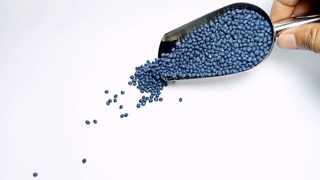 Pouring dark blue masterbatch granules into a white background medium with a stainless scoop, suitable for videography design of plastic industry company profiles	
