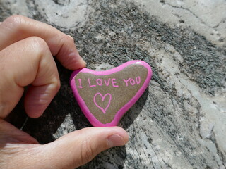 I love you heart shaped rock held in fingers on old marble stone surface