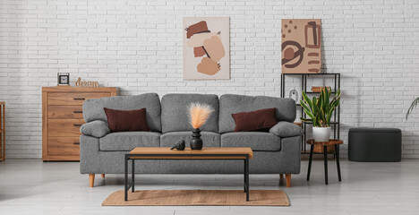 Interior of living room with comfortable grey sofa and table near white brick wall