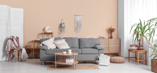 Comfortable sofa, table and magazine holder near beige wall in interior of living room