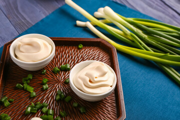 Bowls of tasty sour cream and sliced green onion on blue wooden background