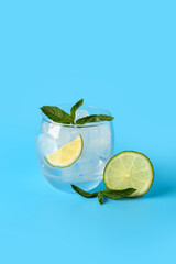 Glass of ice cubes with lime slices and mint on blue background