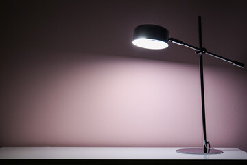 Glowing lamp on table near beige wall in dark room