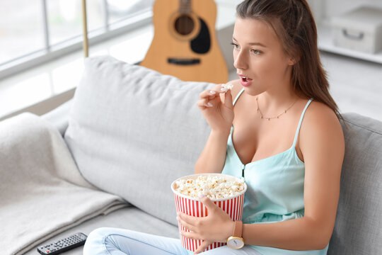 Young woman with popcorn watching TV on her day off at home