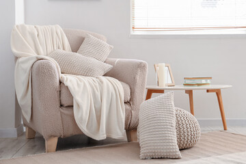 Cozy armchair with cushions and blanket in interior of light living room