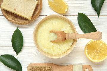Bowl of lemon body scrub with massage brush and soap on white wooden background