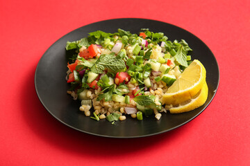 Plate with delicious tabbouleh salad and lemon slices on red background, closeup