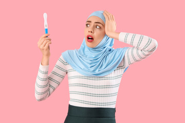 Beautiful shocked Muslim woman with pregnancy test on pink background