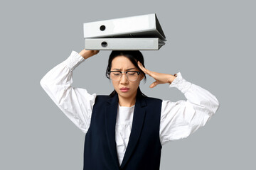 Portrait of tired Asian businesswoman with office folders on grey background