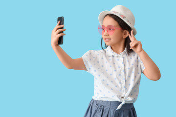 Portrait of fashionable little girl taking selfie on blue background