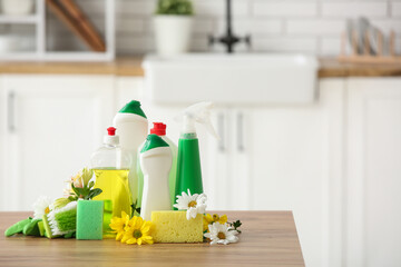 Set of cleaning supplies and spring flowers on wooden table in kitchen