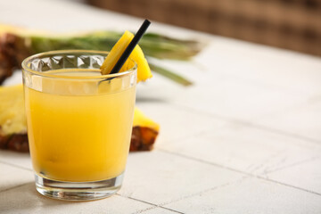 Glass of fresh pineapple juice on tile table near white wall