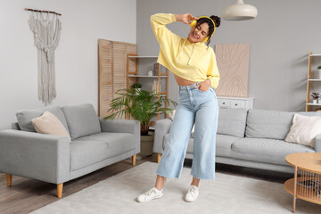 Beautiful young happy African-American woman in headphones listening music and dancing at home
