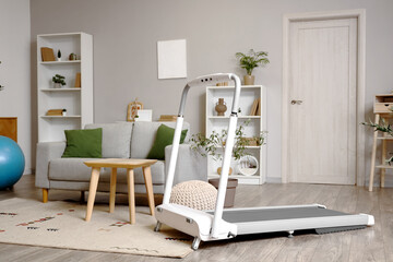 Interior of light living room with treadmill and sofa
