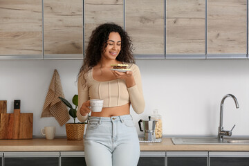 Young African-American woman with bars of chocolate and cup of coffee in kitchen