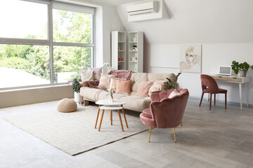 Cozy sofa with cushions, armchair and coffee table with flowers in interior of living room