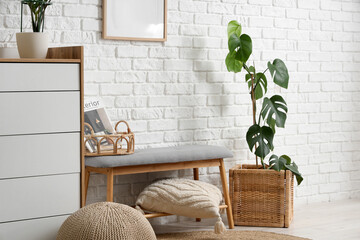 Comfortable grey bench, chest of drawers and pouf near white brick wall in interior of room, closeup