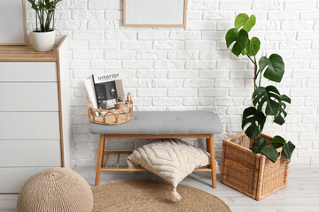 Comfortable grey bench, chest of drawers and cushion near white brick wall in interior of room,...