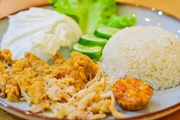 Close up view of Ayam Geprek on the plate with rice, lettuce leaf, cabbage and sliced of cucumber. Typical Indonesian fried chicken dish with flour that is mashed or mashed with plow chili. 