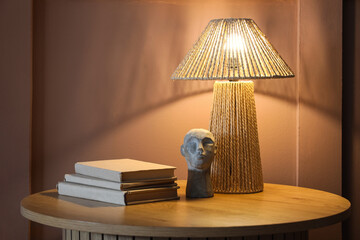 Glowing lamp with statuette and books on table near brown wall