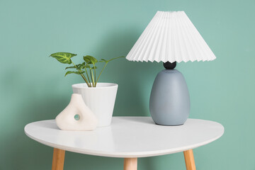 Stylish lamp with plant and vase on table near green wall