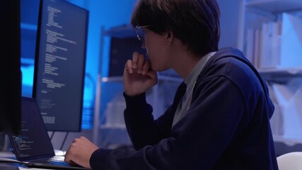 Young Asian male software developer focused coding on multiple screens in modern technology office environment - Powered by Adobe