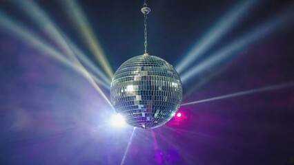 Fototapeta premium Close-up of a shimmering disco ball suspended in a dark room with colorful beams of light, evoking a retro night party atmosphere filled with motion, music, dancing and classic nightlife nostalgia