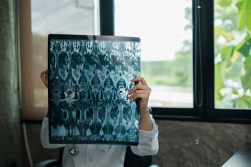 A healthcare worker holds up an X-ray image in a well-lit clinic, with a view of greenery through...