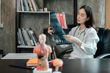 Female doctor examines X-ray in a contemporary office setting, surrounded by medical books and...
