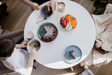 Family breakfast with cake and fruit on table, cozy home moment, kids eating, Sphynx cat nearby