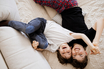 Two happy brothers laughing and hugging on bed, joyful childhood moment, family love at home