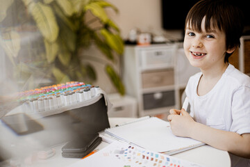 Smiling boy drawing with colorful markers at home, surrounded by sketchbook and art supplies