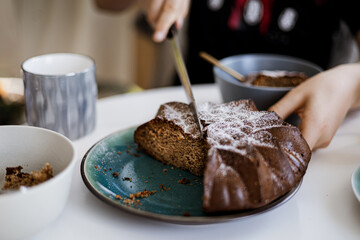 Hand cutting homemade cake on plate, cozy breakfast scene with cups and bowls on table