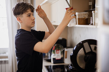 Teenage boy in black t-shirt reaching for a jar on a kitchen shelf, home cooking scene