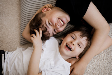 Two happy brothers laughing and hugging while lying on the floor, enjoying playful moment