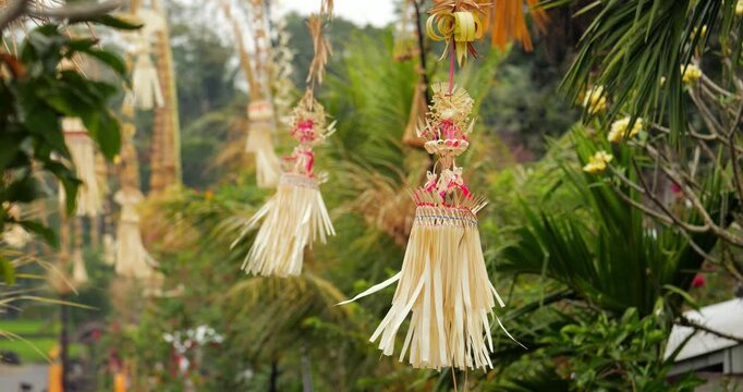 Rather large sampian decorations hanging on penjor poles at street of Balinese village, medium telephoto slow motion shot. Hand made ornamental slowly sway on wind