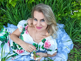 Beautiful blonde woman enjoying a sunny day outdoors while posing gracefully in a floral dress...