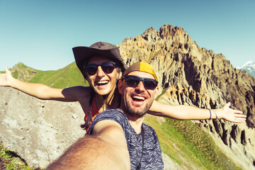 Smiling couple of hikers friends taking selfie on top of mountain. Millennial guy girl enjoying summertime day out trip laughing at camera together - Millennial travelers standing in scenic nature