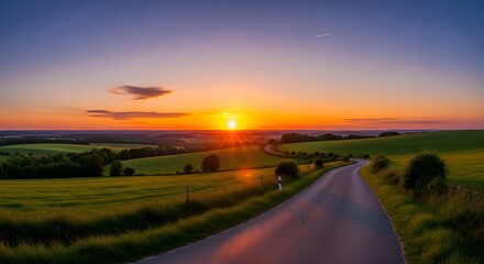 Fototapeta premium Winding Road Through Verdant Fields at Sunset, with a Contrail in the Sky