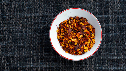 Red chili flakes, red pepper flakes, in a white porcelain sauce cup, placed on grey fabric napkin. In cozy home environment