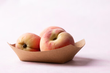 Fresh peaches in paper bowl on pink background, Summer fruit